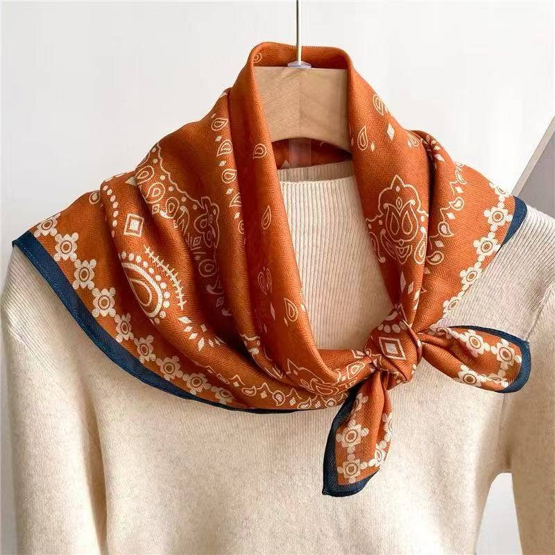 Foulard quadrato arancione con bordo blu annodato al collo sopra un maglione avorio