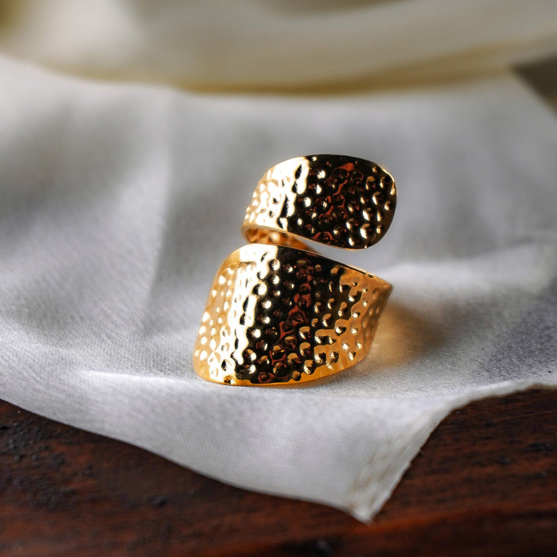 Anello Seizan in acciaio inossidabile placcato oro, superficie martellata, su tessuto bianco e legno scuro